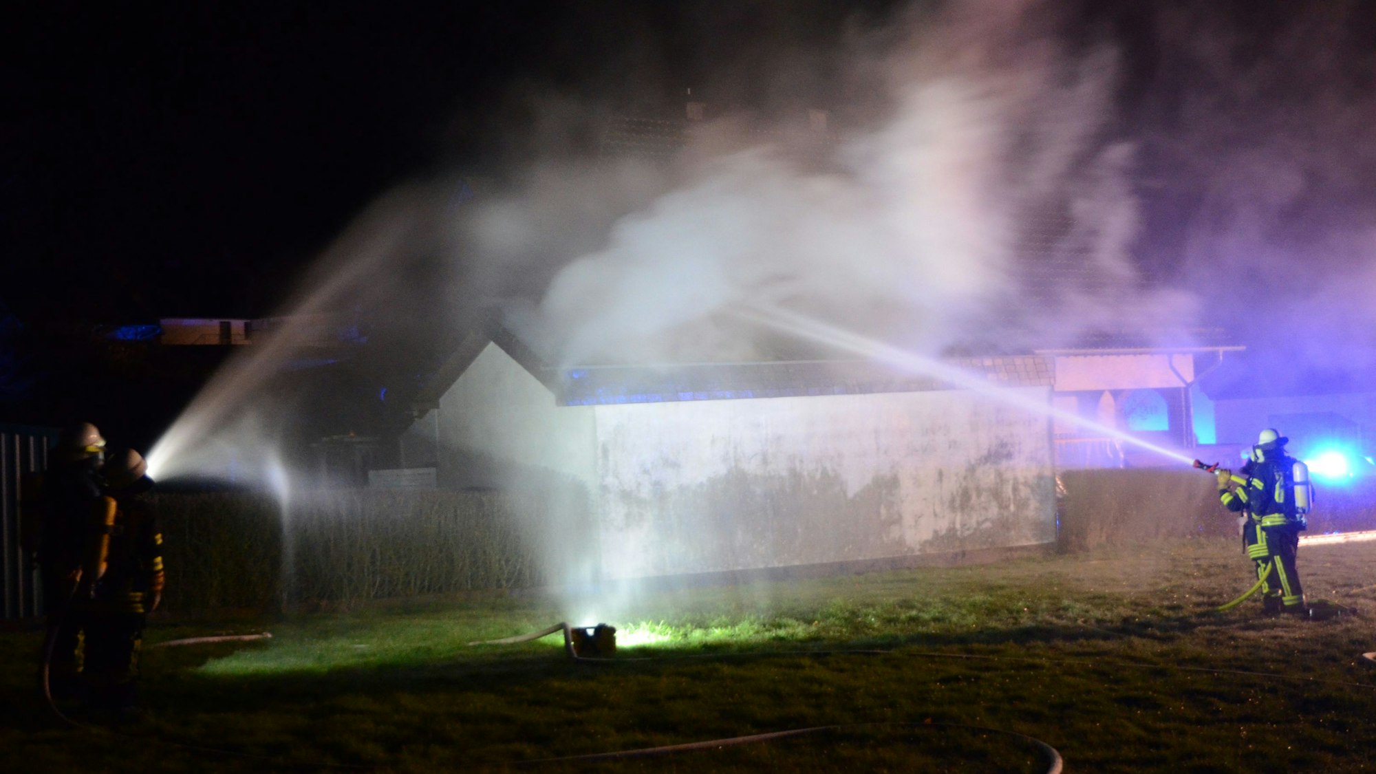 Feuerwehrleute löschen mit Strahlrohren die brennende Garage an einem Wohnhaus in Herhahn.