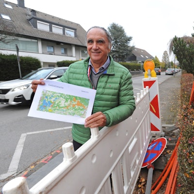 Reiner Pliefke steht mit Karte zum Novanetz-Ausbau an einer Baustelle mit orangenen Glasfaser-Kabeln.