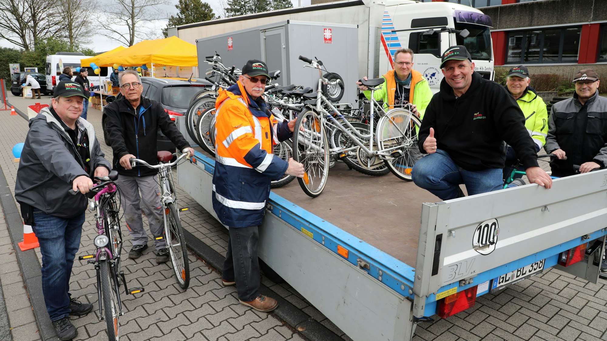 Männer sitzen mit Fahrrädern auf einem Hänger.