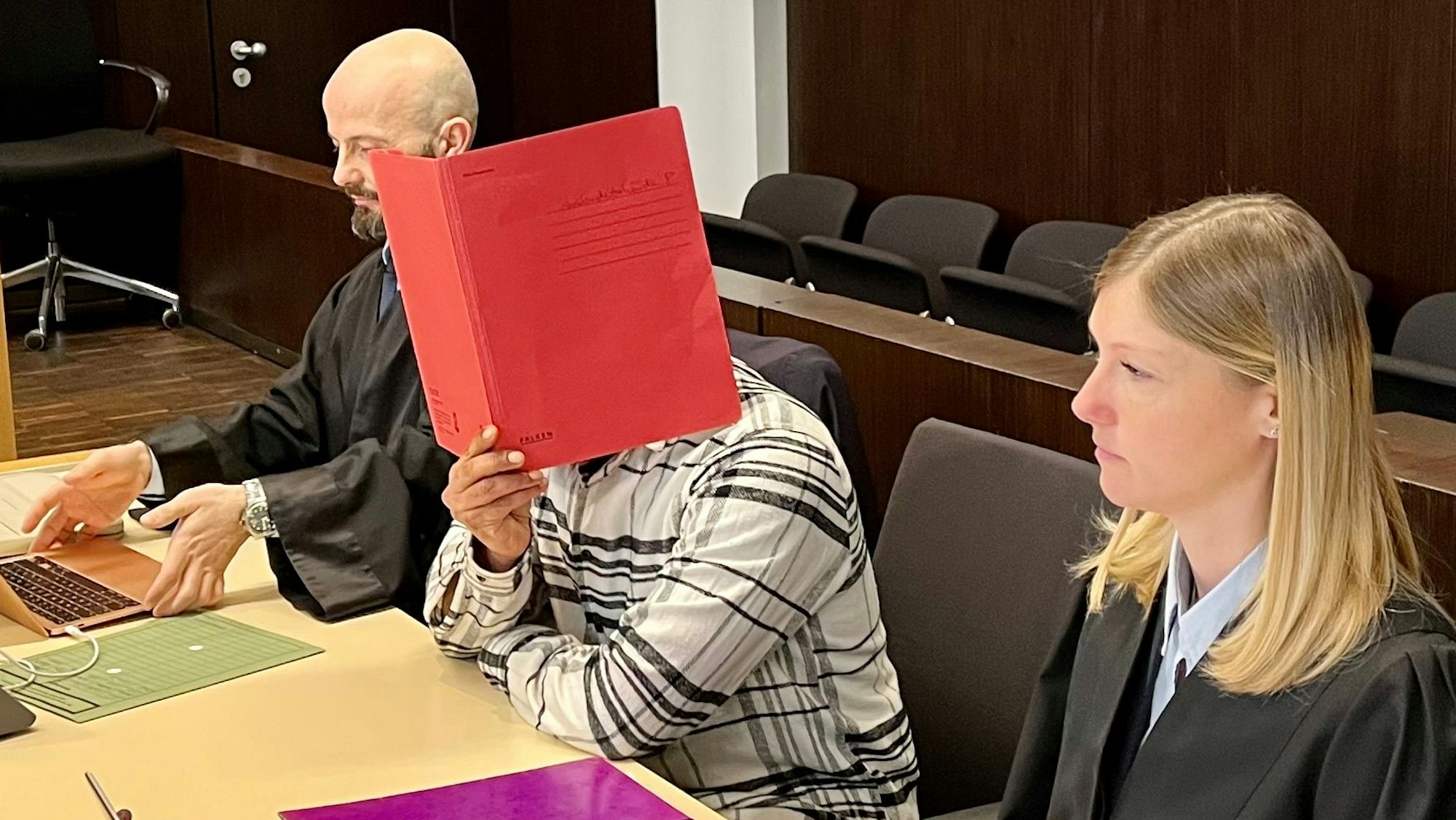 Angeklagter Roma aus Opladen mit Verteidigern vor dem Landgericht Düsseldorf. Er versteckt sich hinter einem roten Aktendeckel.