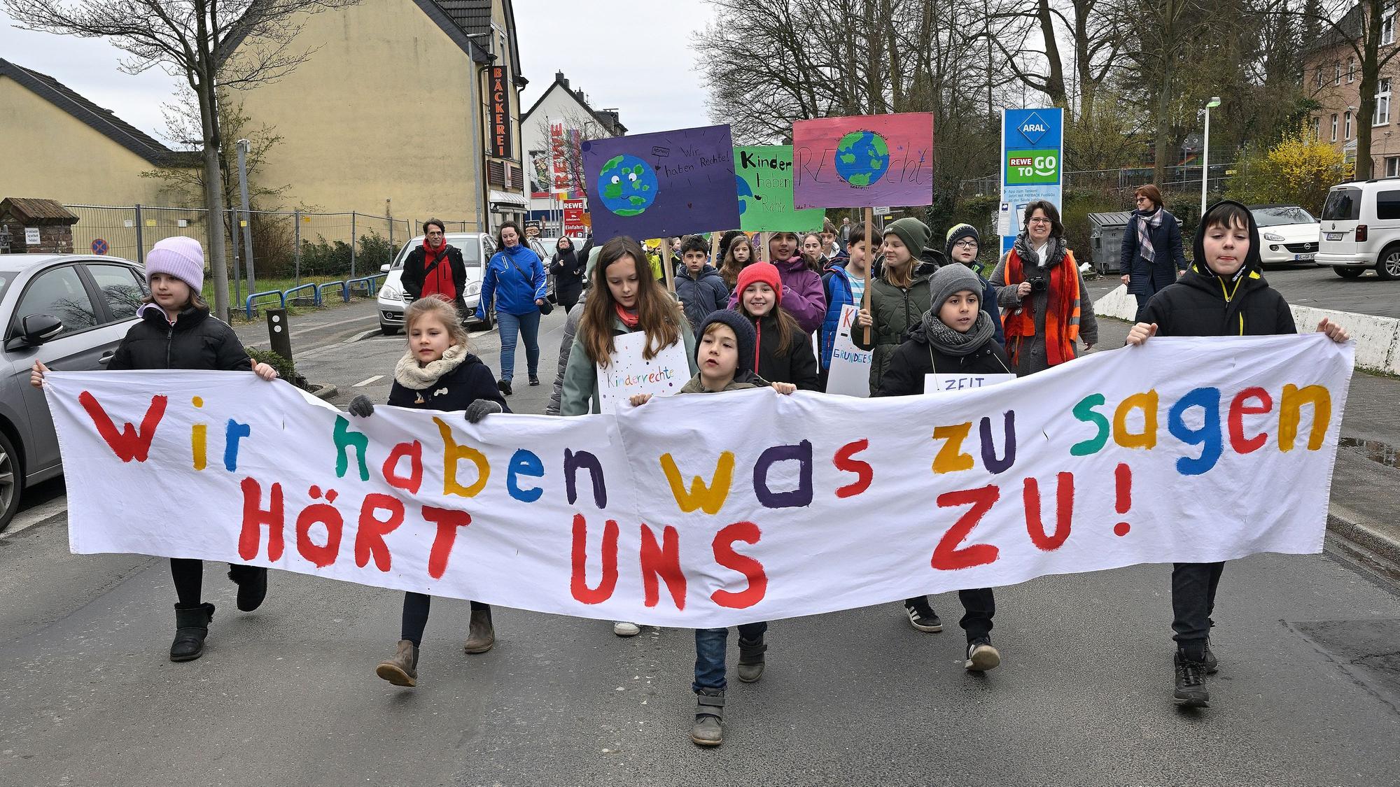 Kinder laufen auf der Straße und halten ein Banner mit der Aufschrift „Wir haben was zu sagen, hört uns zu“.