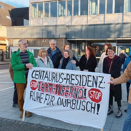 Einige Personen demonstrieren vor dem Rathaus. Sie halten ein Banner, auf dem steht: „Centaurus-Residenz: Lärm-Inferno! Ruhe für Durbusch!“