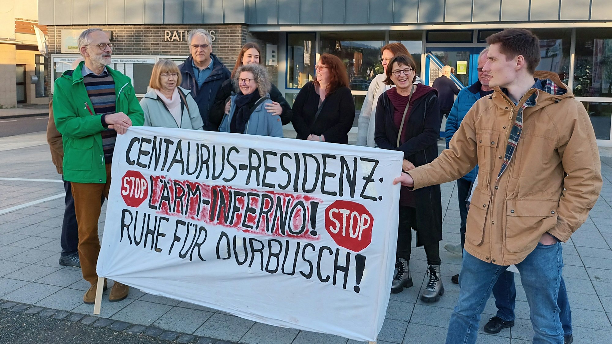 Einige Personen demonstrieren vor dem Rathaus. Sie halten ein Banner, auf dem steht: „Centaurus-Residenz: Lärm-Inferno! Ruhe für Durbusch!“