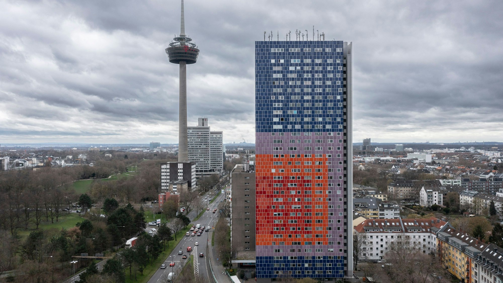 Das Hochhaus steht an einer befahrenen Straße bei bewölktem Himmel.