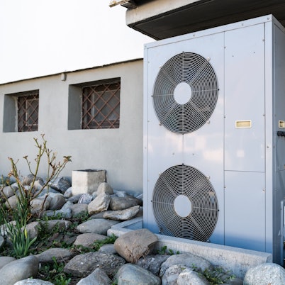 Die Lüftungsanlage einer Wärmepumpe steht vor einem Wohnhaus.