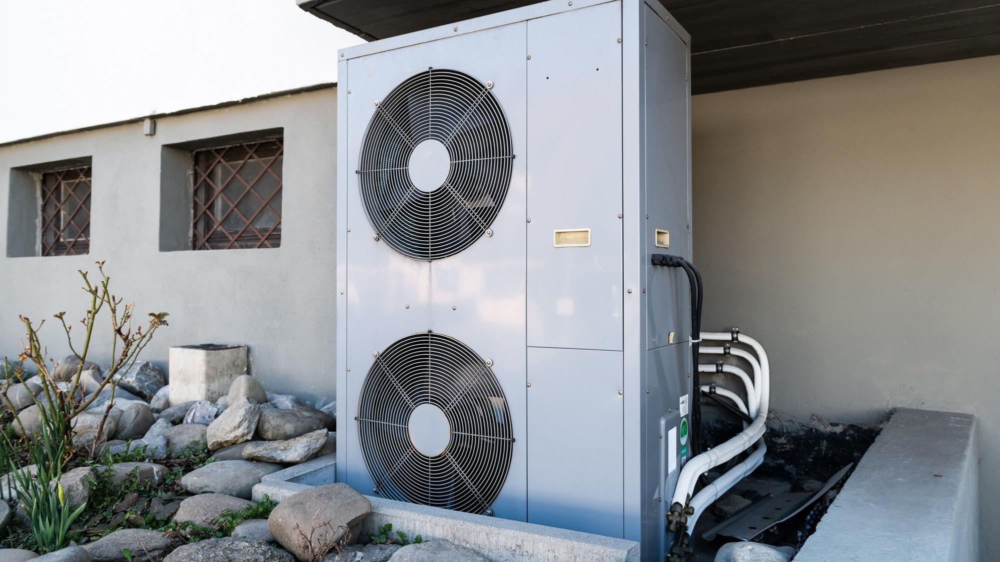 Die Lüftungsanlage einer Wärmepumpe steht vor einem Wohnhaus.