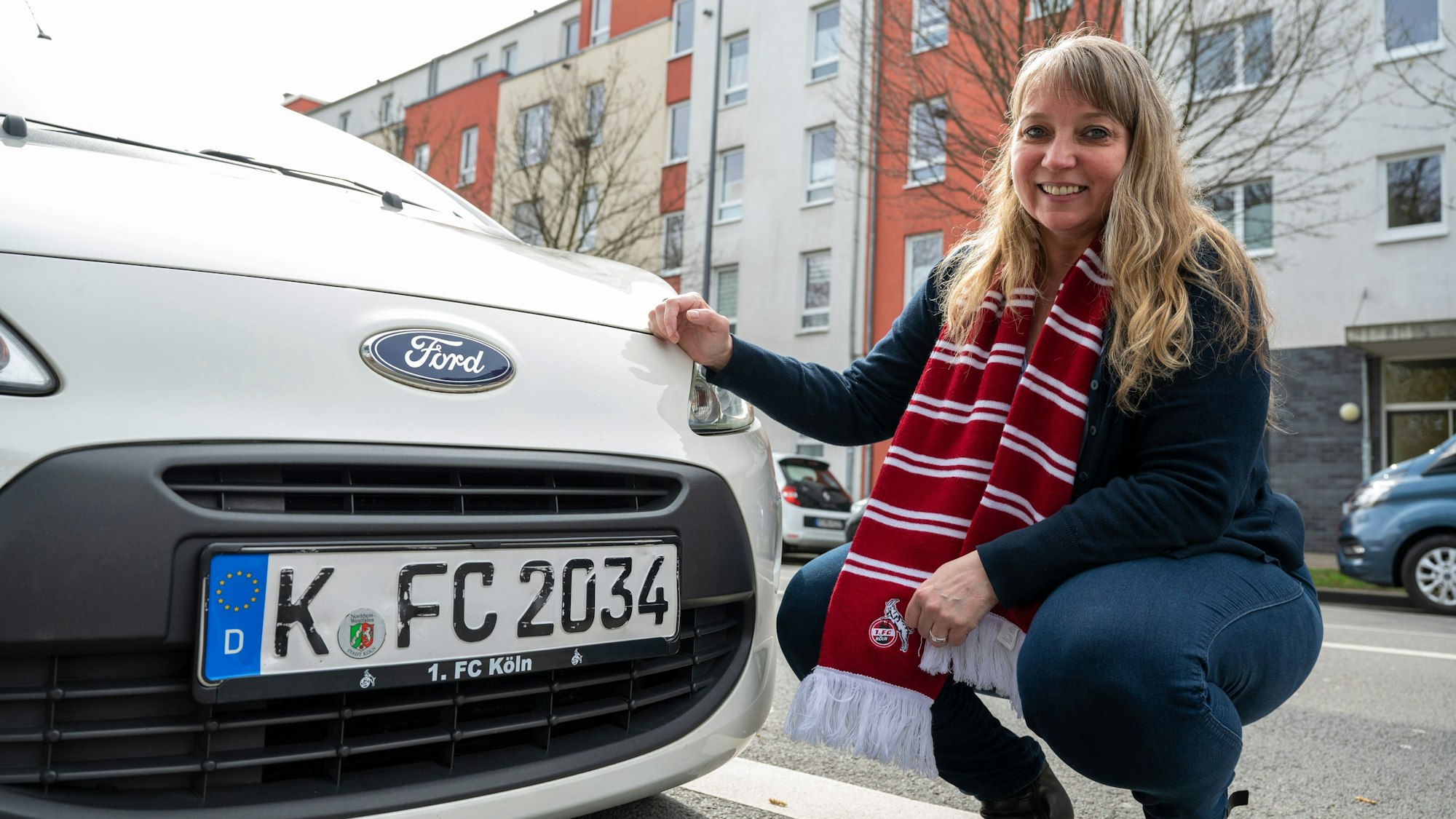 Eine Frau kniet neben ihrem Auto, man sieht das Kennzeichen.