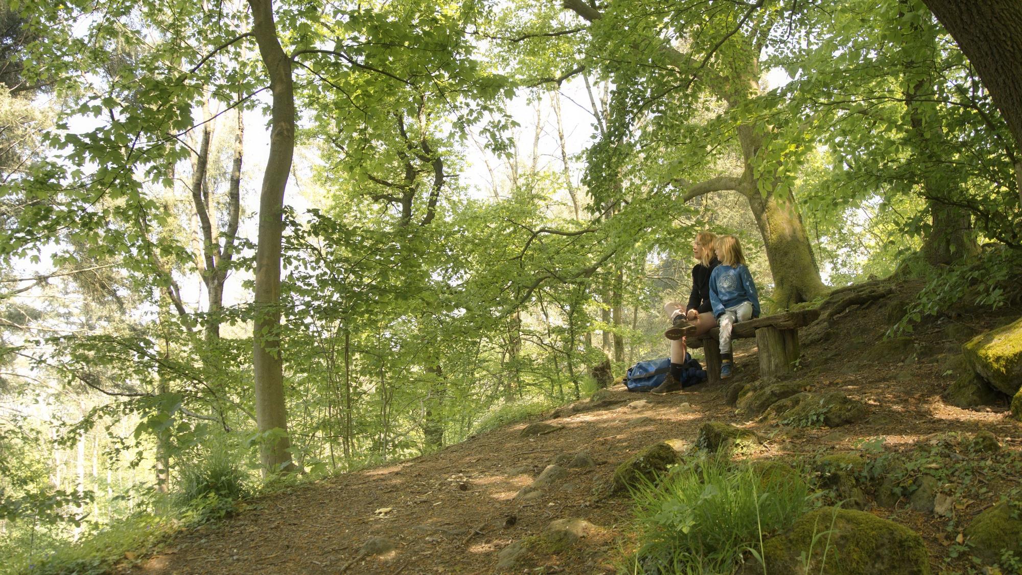 Eine Mutter und ihr Sohn sitzen auf der Bank des Kleinen Oelbergs im Siebengebirge.