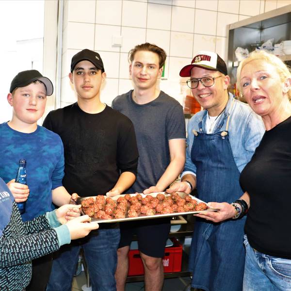 Vier Jungen, ein Mann und eine Frau halten eine Platte mit Hackbällchen in die Kamera