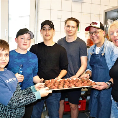 Vier Jungen, ein Mann und eine Frau halten eine Platte mit Hackbällchen in die Kamera