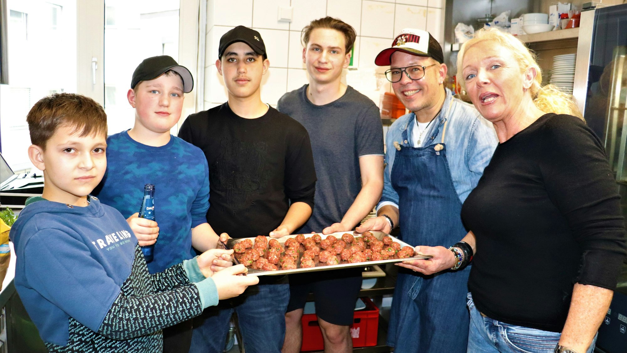 Vier Jungen, ein Mann und eine Frau halten eine Platte mit Hackbällchen in die Kamera