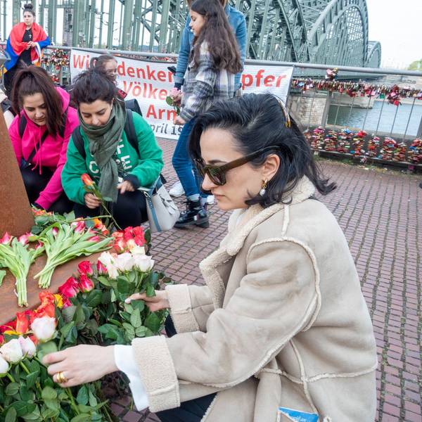 Erinnerung an den Genozid an Armeniern am Heinrich-Böll-Platz: Eine Frau mit Sonnenbrille legt Blumen vor einer Gedenkstele ab. Im Hintergrund ist die Hohenzollernbrücke zu sehen.