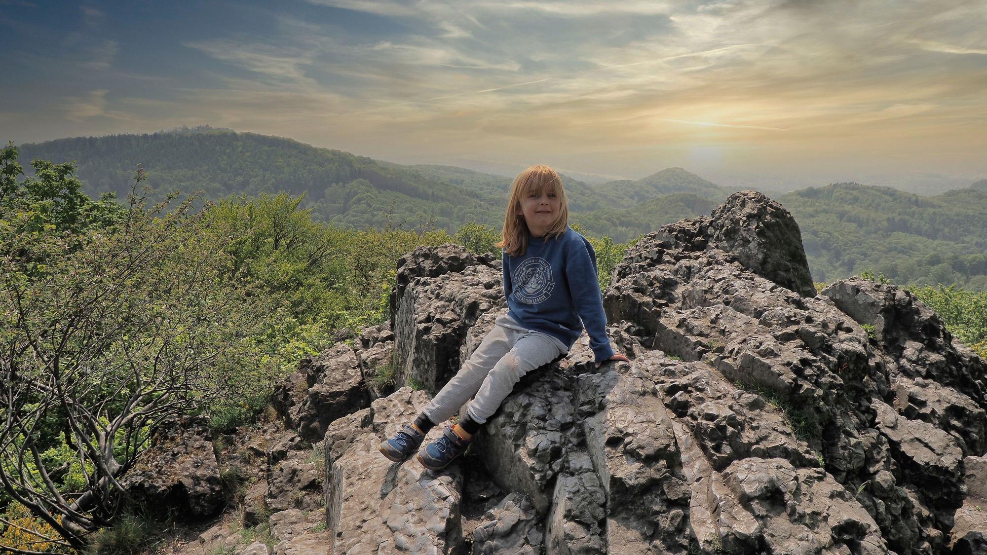Ein Junge sitzt auf einem Felsen, im Hintergrund ist das Panorama des Siebengebirges zu sehen.