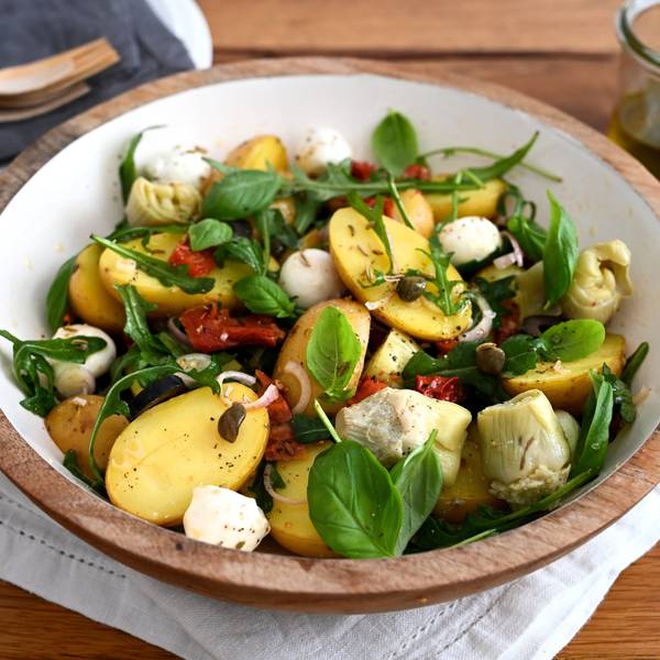 In einer Schüssel sind Kartoffeln, Rucola, Mozzarella, Artischocken, Oliven und getrocknete Tomaten zu einem Salat zubereitet.