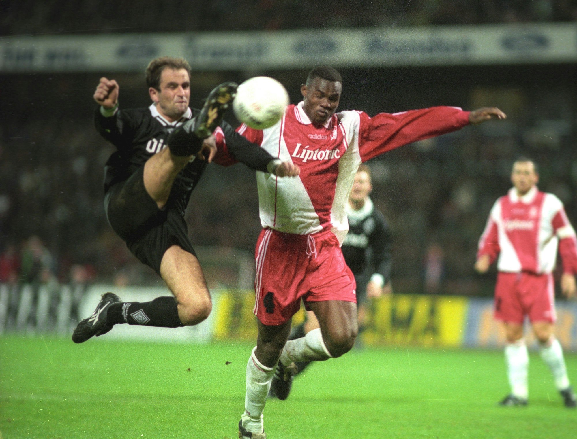 Zwei Fußballer kämpfen um den Ball. Einer ist ganz in schwarz gekleidet, der andere in Rot und Weiß.