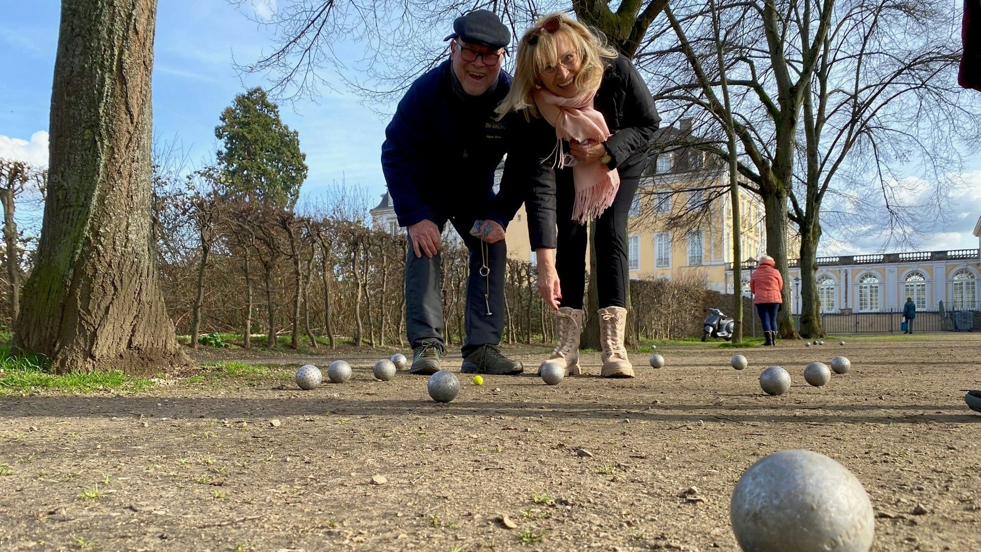 Zwei Menschen spielen Boule in einem Park.