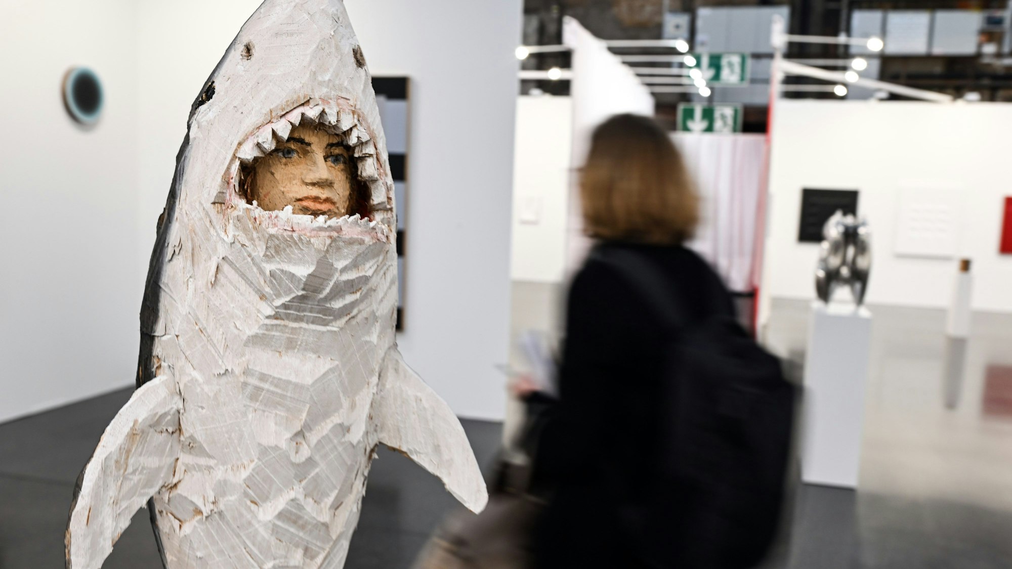 Ausstellungsbesucher gehen durch die Messehalle der Kunstmesse Art Düsseldorf, links das Werk Figurensäule Hai von Stephan Balkenhol.
