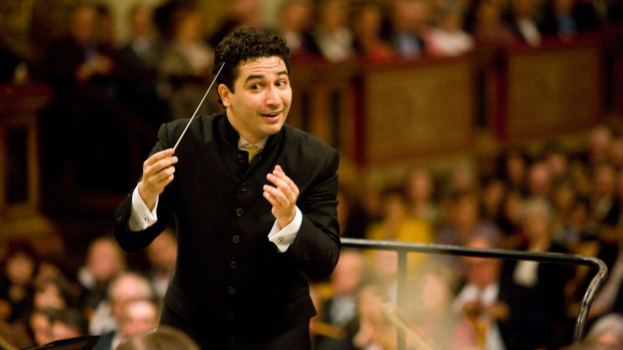 Andrés Orozco-Estradadirigitert mit einem Lächeln und hat einen Taktstock in der rechten Hand. Er trägt schwarze Kleidung.