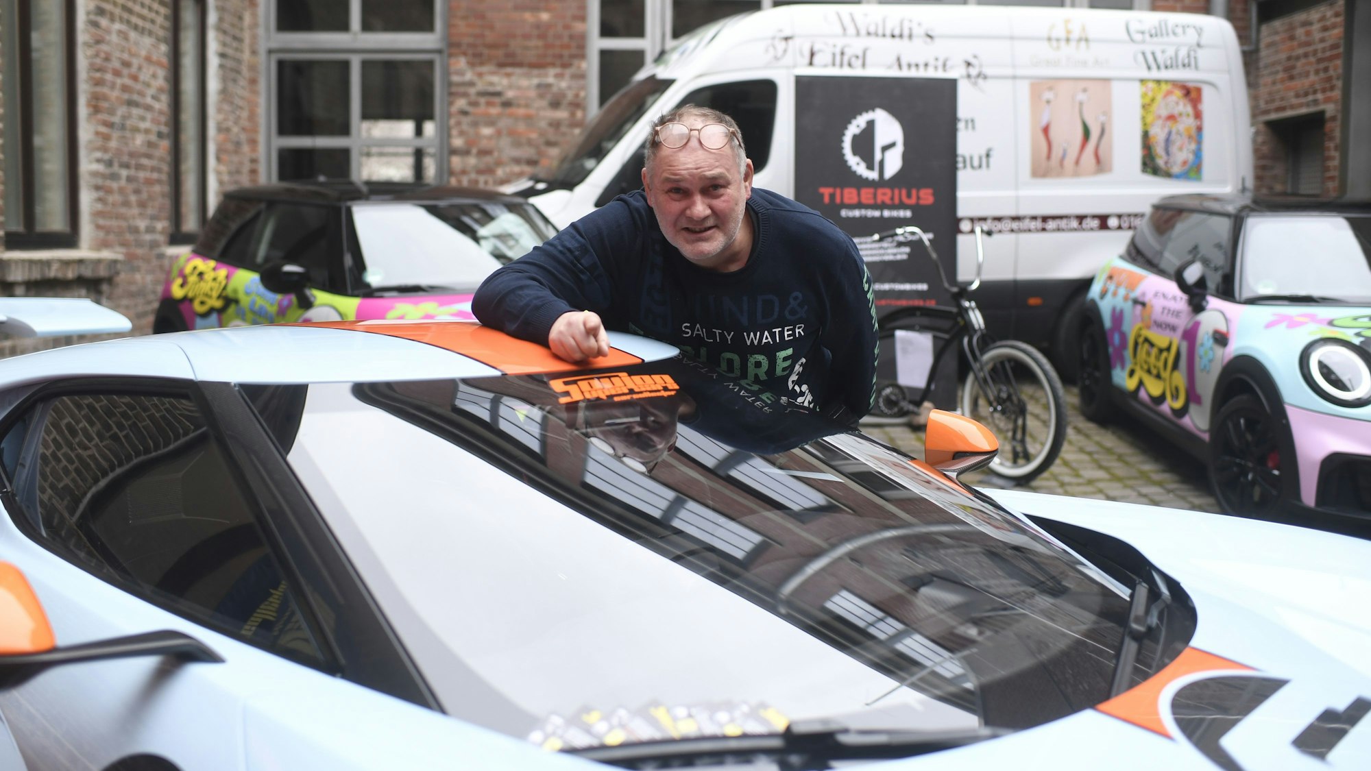 80-Euro-Waldi (Walter Lehnertz) steht an einem Sportwagen vor seiner neuen Galerie in Euskirchen.