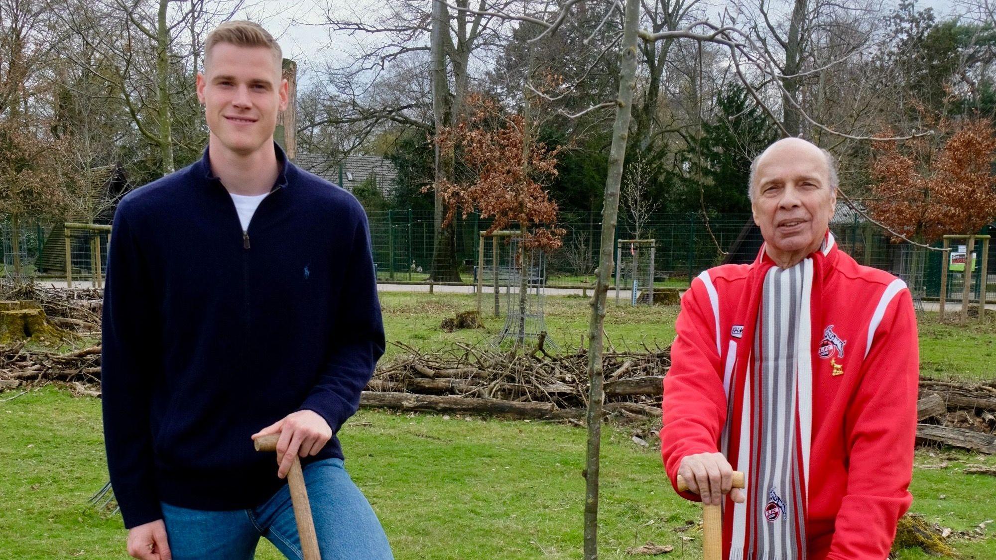 Zwei Männer stehen mit einer Schaufel in der Hand neben einem neu gepflanzten Baum.
