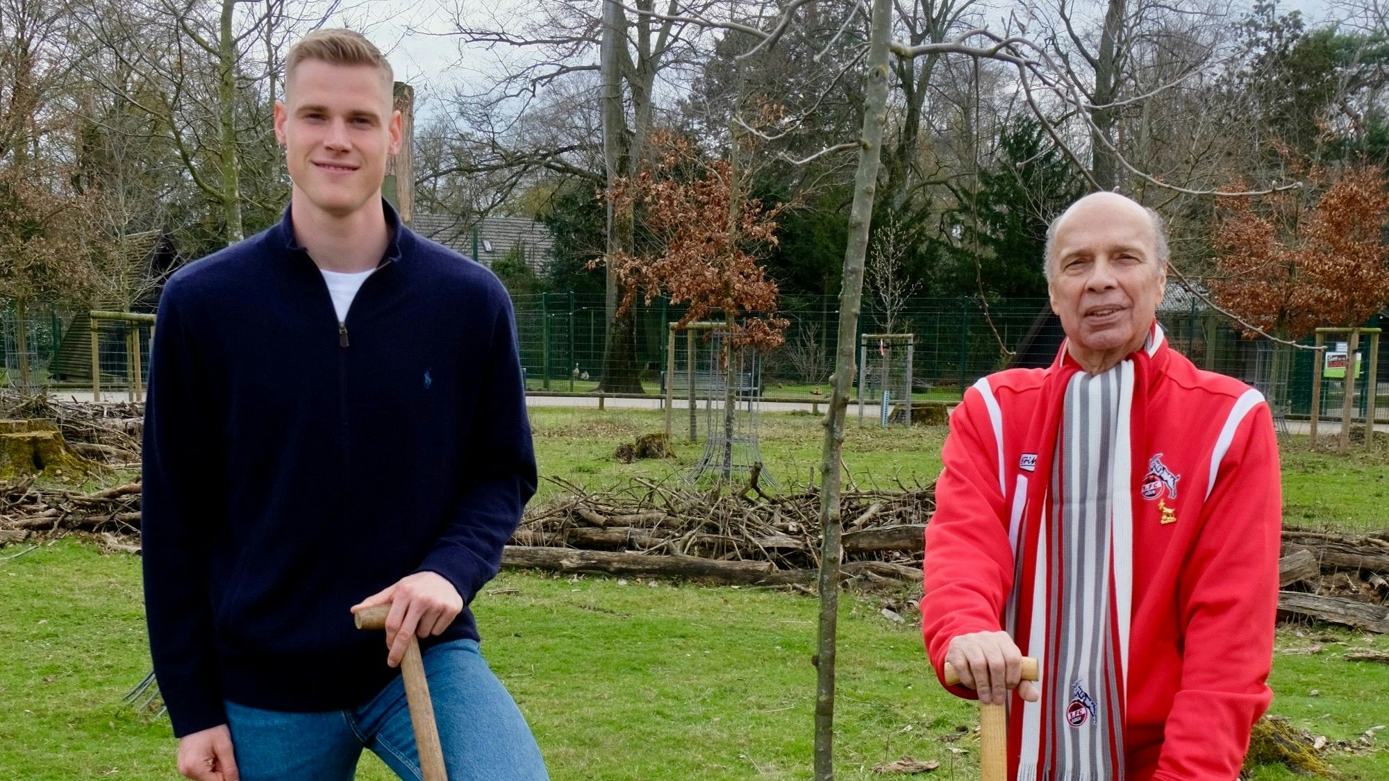 Zwei Männer stehen mit einer Schaufel in der Hand neben einem neu gepflanzten Baum.