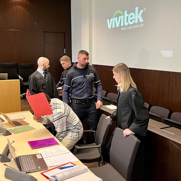 Ein Mann, der sich einen Aktendeckel vors Gesicht hält, setzt sich im Landgericht Düsseldorf.