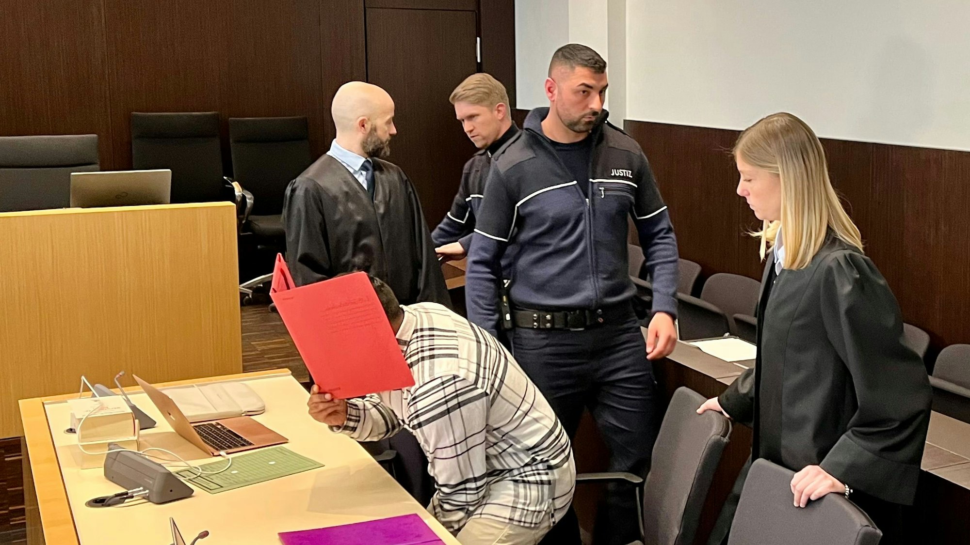 Der Angeklagte, der am 5. November 2022 in Düsseldorf mit dem Auto in eine Menschenmenge gefahren sein soll, setzt sich im Saal E.131 des Düsseldorfer Landgerichts. Er hat einen Aktendeckel vor dem Gesicht.