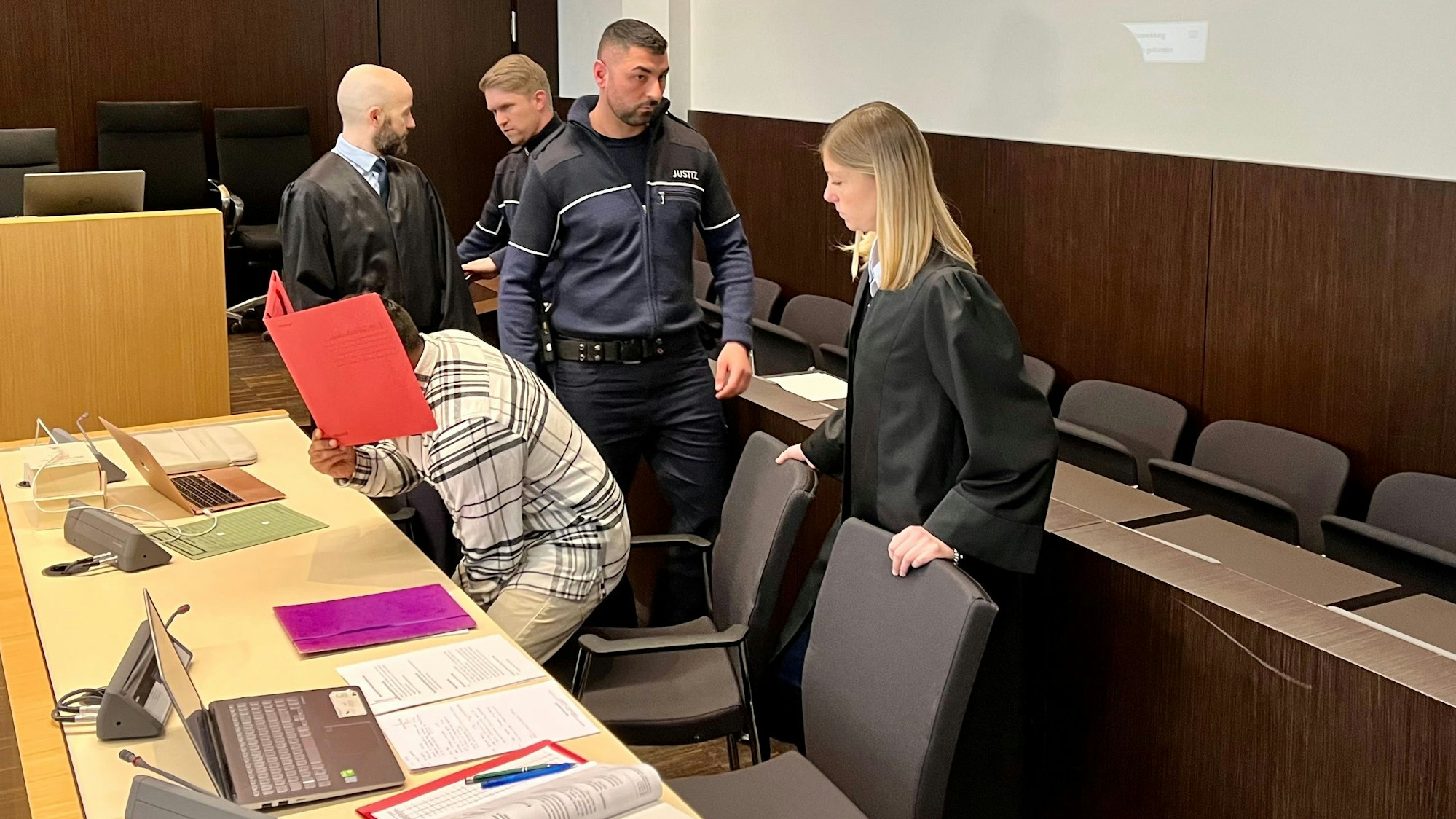 Ein Mann, der sich einen Aktendeckel vors Gesicht hält, setzt sich im Landgericht Düsseldorf.