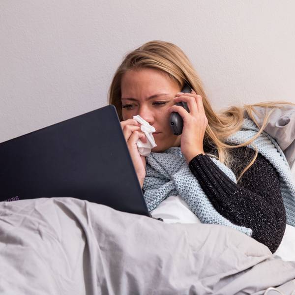 Eine Frau führt aus dem Bett in Telefonat am Handy.