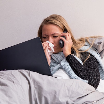 Eine Frau führt aus dem Bett in Telefonat am Handy.