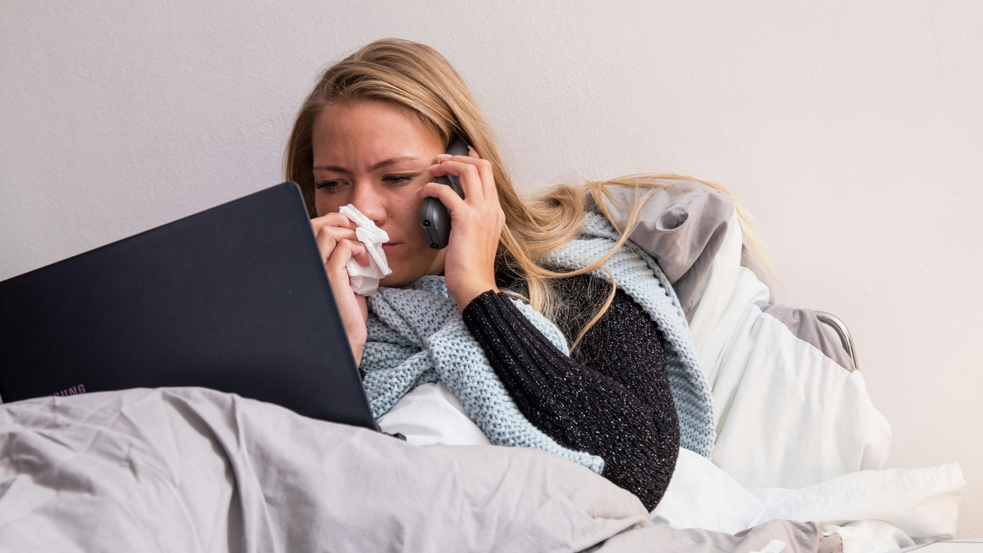 Eine Frau führt aus dem Bett in Telefonat am Handy.