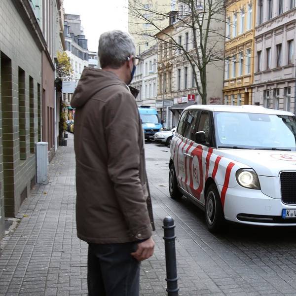 Ein Mann wartet auf ein KVB-Taxi, es ist weiß und rot.