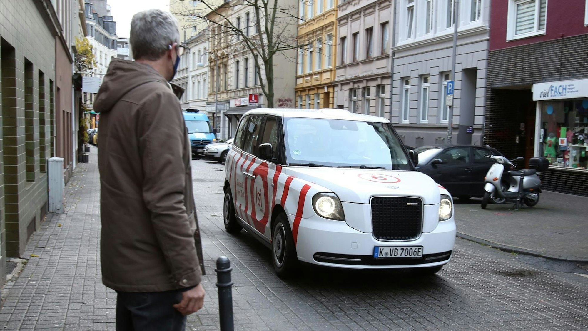 Ein Mann wartet auf ein KVB-Taxi, es ist weiß und rot.