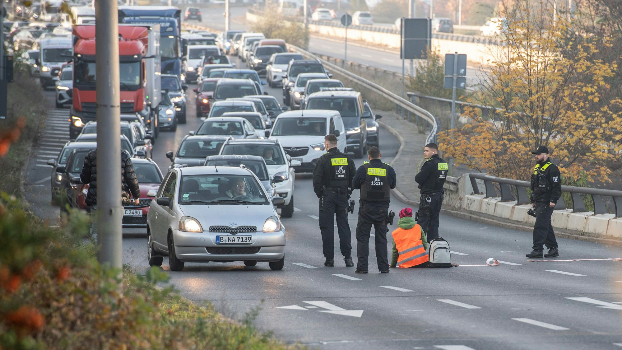 Eine Demonstrantin der Gruppe "Letzte Generation" sitzt, umringt von Polizeibeamten, auf der Ausfahrt der Stadtautobahn am Sachsenring.