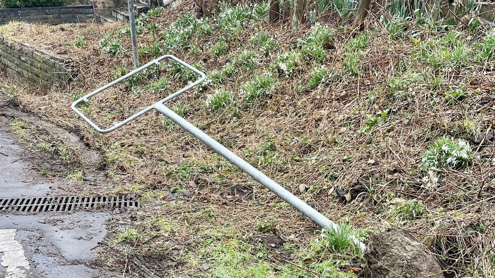 Der Rahmen eines Ortsschildes liegt auf der Wiese im Schlamm.
