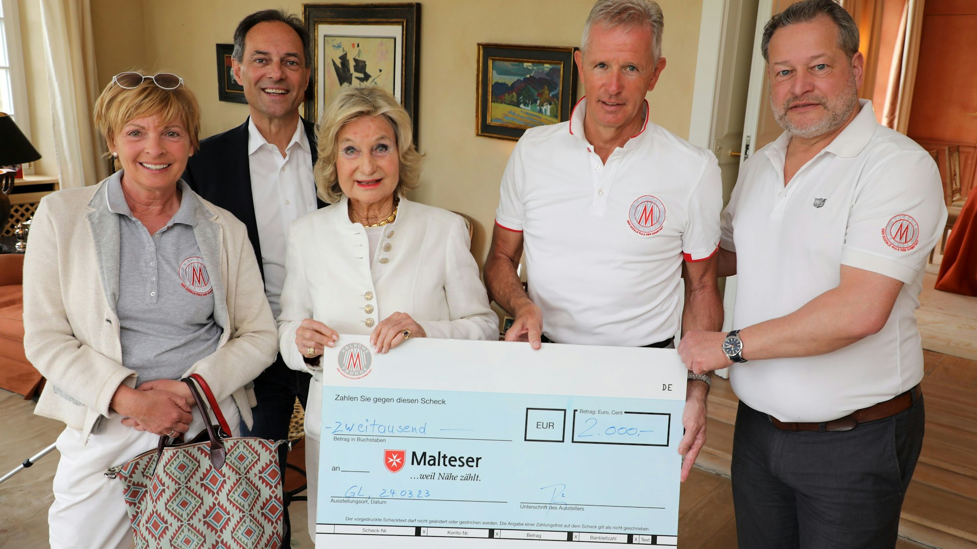 Mehrere Menschen stehen im Wohnzimmer auf dem Igeler Hof bei Bergisch Gladbach und halten einen Scheck in den Händen über 2000 Euro.