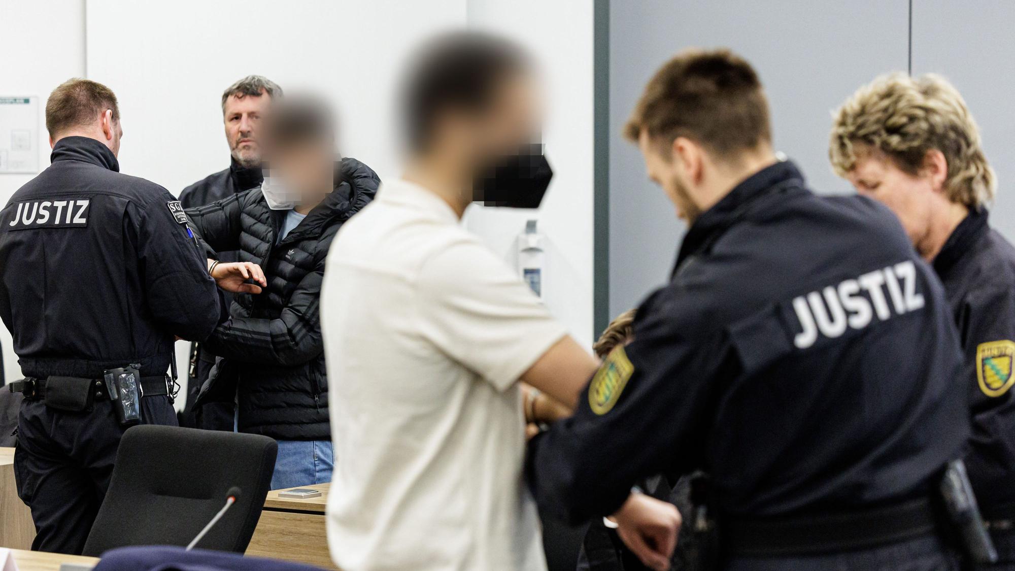 Die Angeklagten Mohamed R. (3.v.r.) und Bashir R. (3.v.l.) werden von Justizbeamten in Handschellen in den Gerichtssaal des Oberlandesgerichts Dresden geführt.