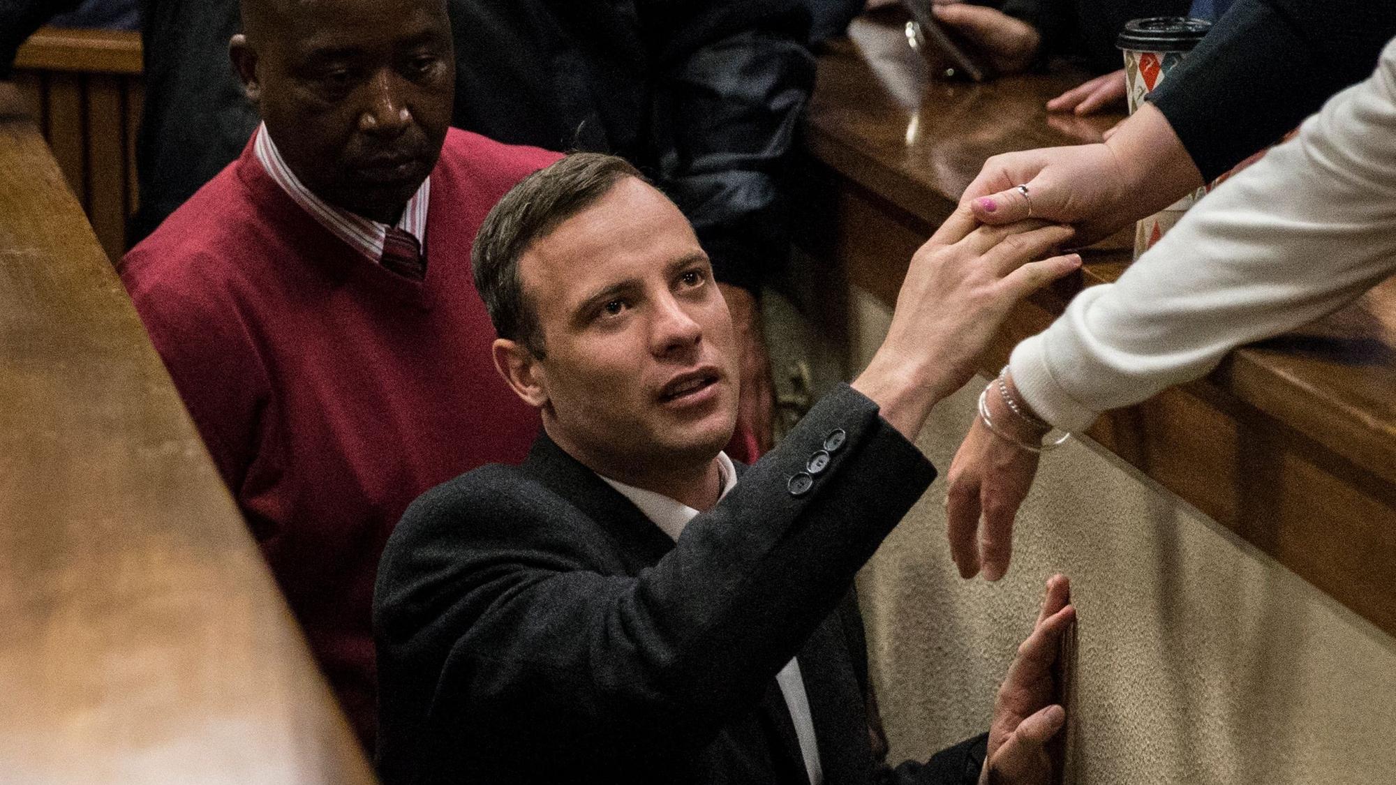 Oscar Pistorius läuft durch den Gang eines Gerichtsaals und ergreift die Hand eines Verbündeten.