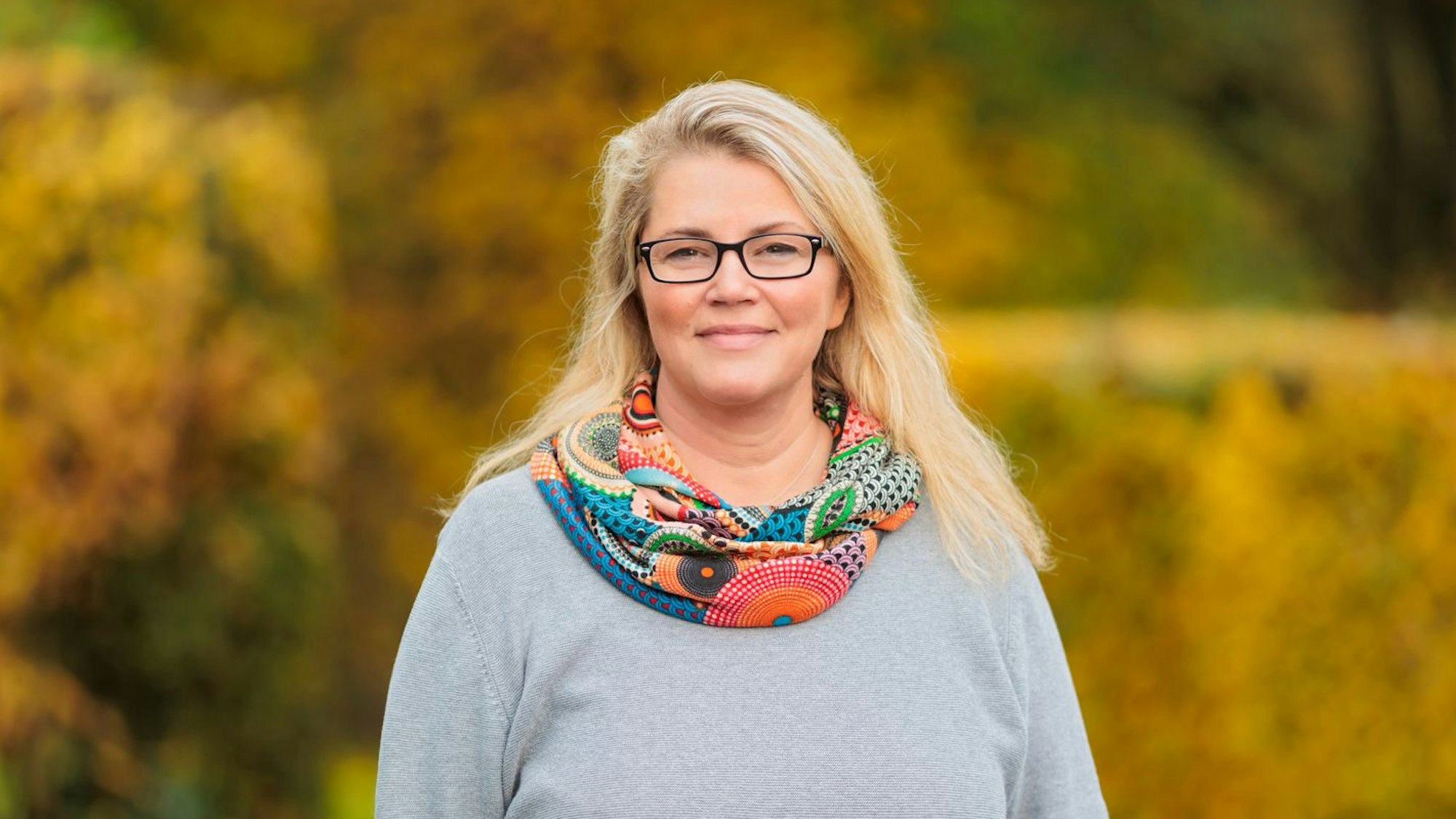 Judith Thies, lange blonde Halle und schwarze Brille, im Porträt.