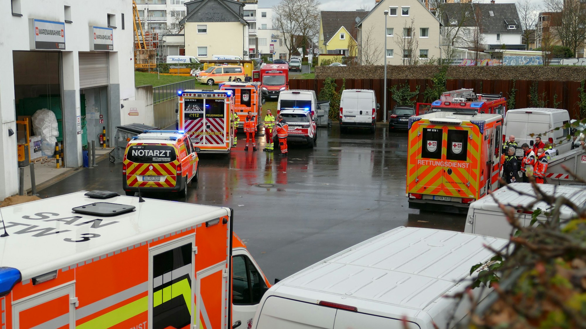 Auf einem regennassen Hinterhof stehen Fahrzeuge von Rettungsdienst und Notarzt, Einsatzkräftee stehen daneben.