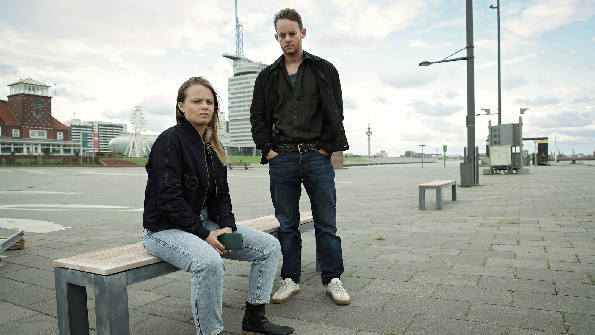Liv Moormann (Jasna Fritzi Bauer) sitzt auf einer Bank auf der Seebäderkaje und schaut nachdenklich. Hinter ihr steht Robert Petersen (Patrick Güldenberg).