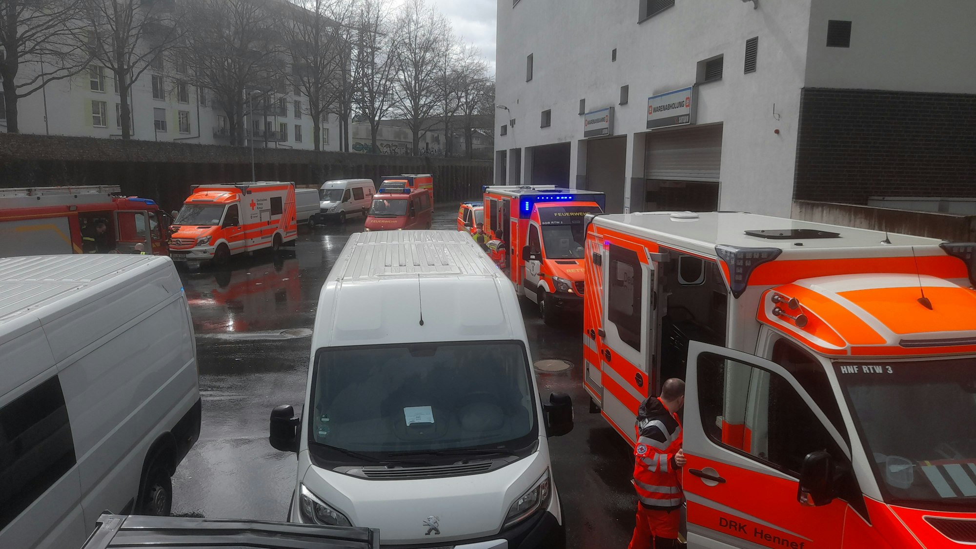 Etliche Rettungsfahrzeuge stehen auf dem Parkplatz neben einem Gebäude, auch zwei Kastenwägen sind dort geparkt.