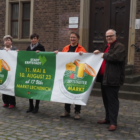 Die zwei Männer und drei Frauen halten das grün-weiße Banner mit dem Logo des geplanten Feierabendmarktes in den Händen.