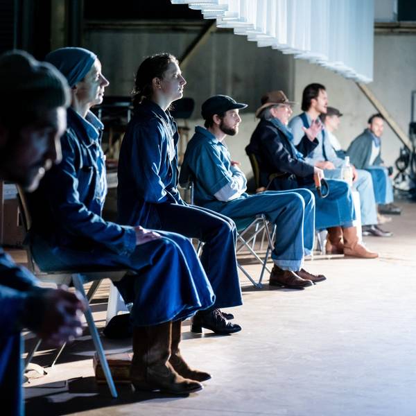 Acht Schauspieler des Kölner Ensembles sitzen, von der Seite fotografiert, nebeneinander auf Klappstühlen im Stück „Früchte des Zorns“ im Depot 2. Sie tragen alle Kostüme aus Jeansstoff.