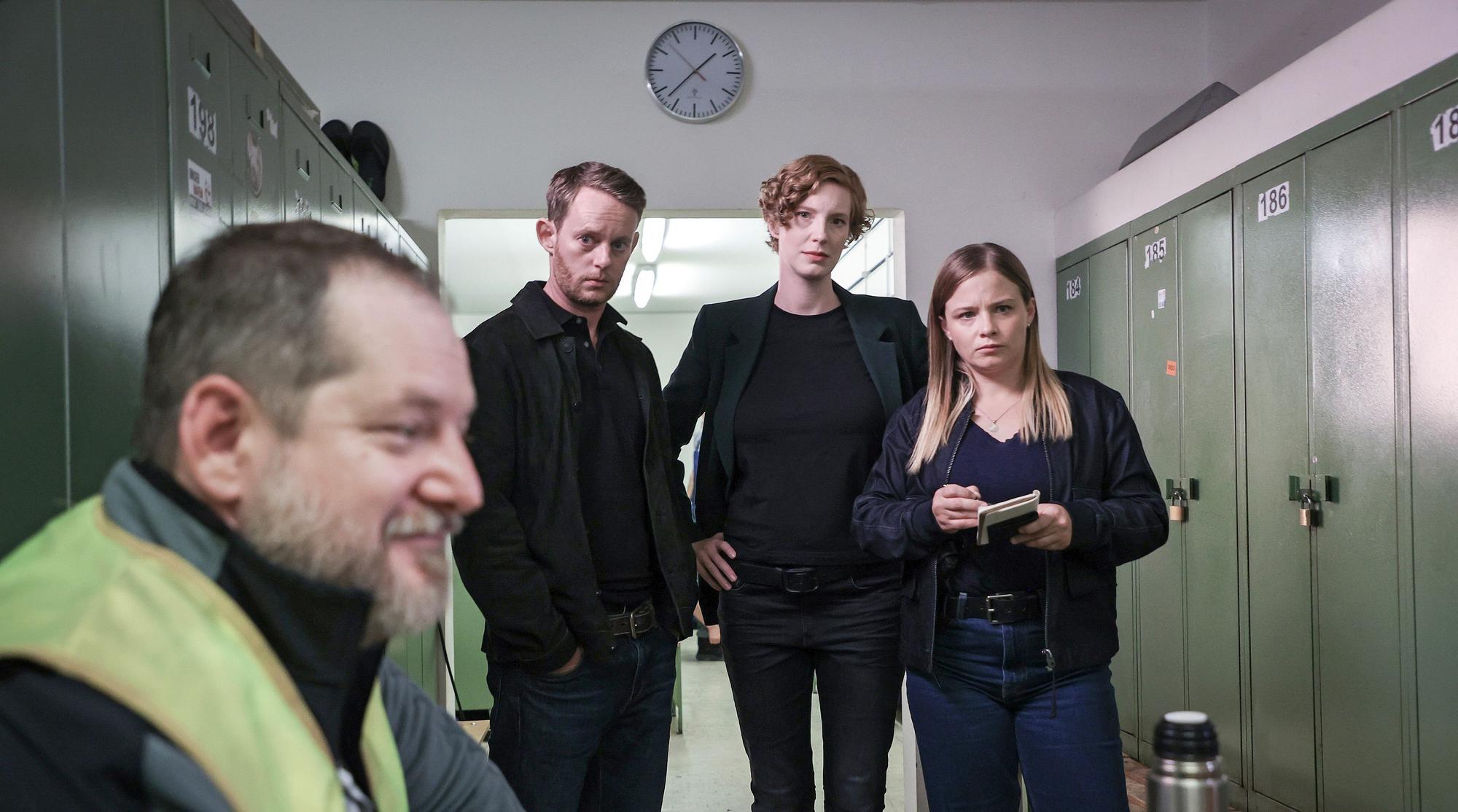Szene aus dem Bremer Tatort Donuts. In einem Spindraum in Bremerhaven stehen das Ermittlungsteam Robert Petersen (Patrick Güldenberg, zweiter von links), Linda Selb (Luise Wolfram, mitte) und Liv Moormann (Jasna Fritzi Bauer) und befragen den Tallyman (Matthieu Svetchine), der verschwommen links im Vordergrund zu sehen ist.