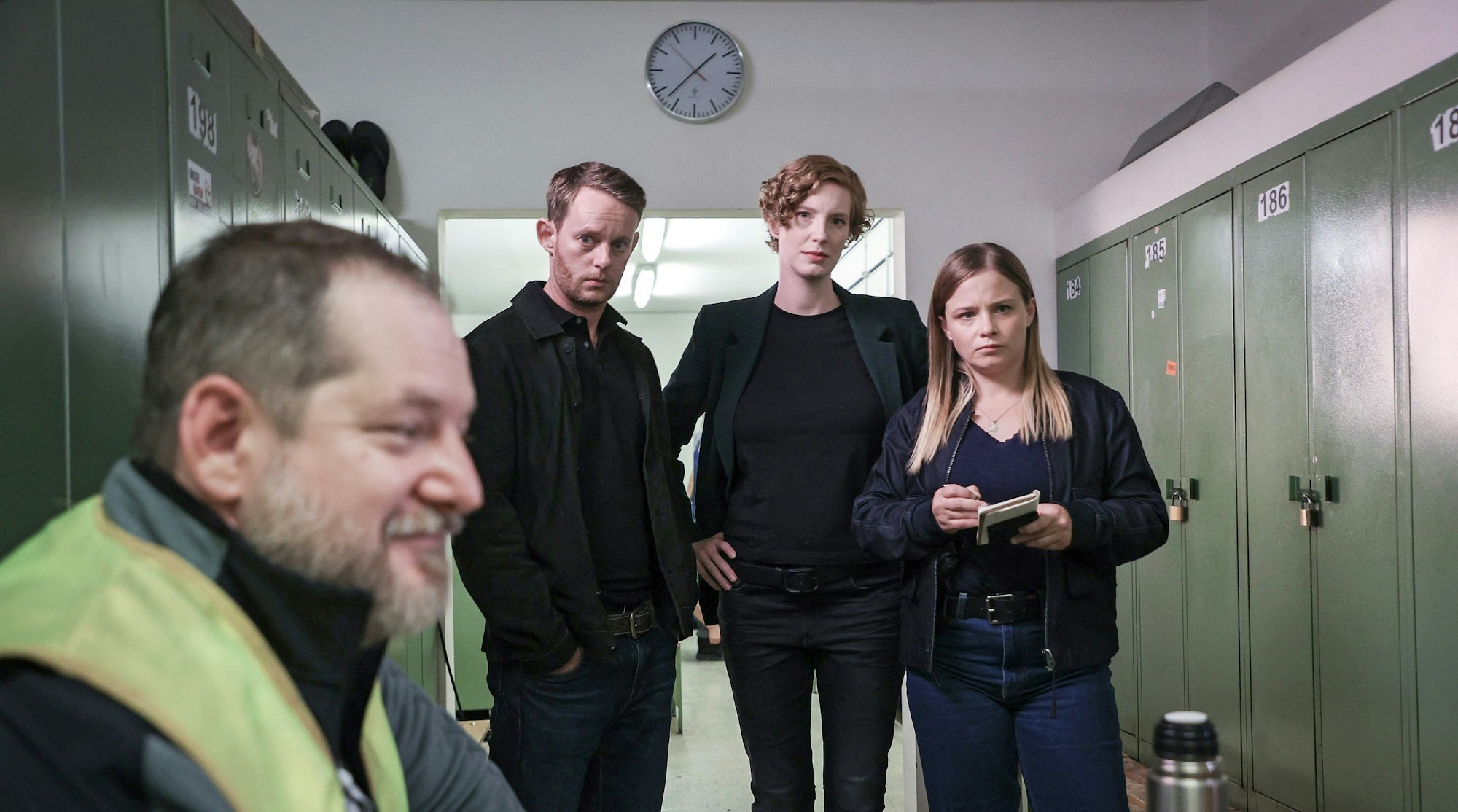 Szene aus dem Bremer Tatort Donuts. In einem Spindraum in Bremerhaven stehen das Ermittlungsteam Robert Petersen (Patrick Güldenberg, zweiter von links), Linda Selb (Luise Wolfram, mitte) und Liv Moormann (Jasna Fritzi Bauer) und befragen den Tallyman (Matthieu Svetchine), der verschwommen links im Vordergrund zu sehen ist.