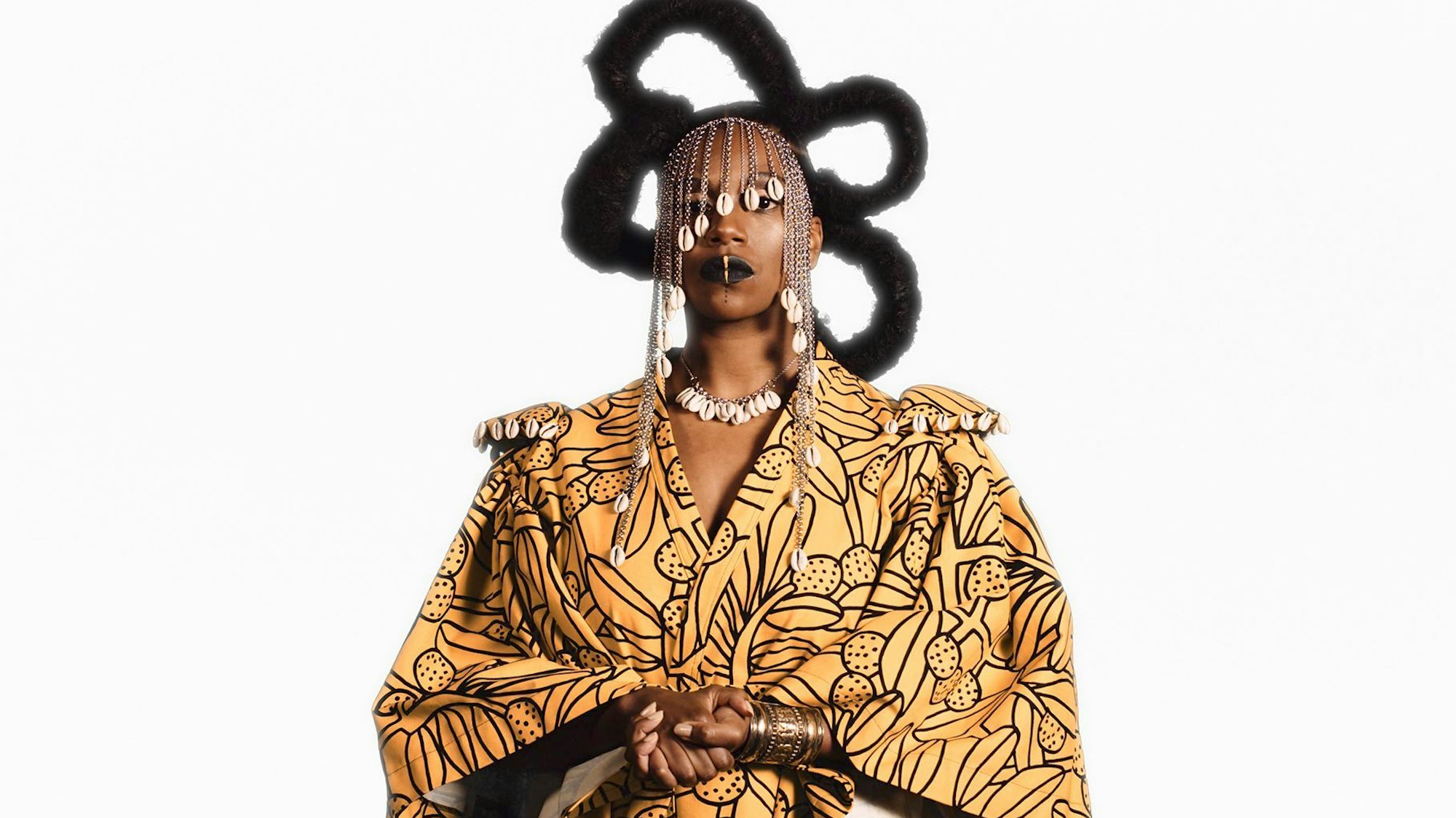 Zu sehen ist eine schwarze Frau mit einem gelben Kleid, sie trägt Schmuck an Kopf, Hals und am Handgelenk.