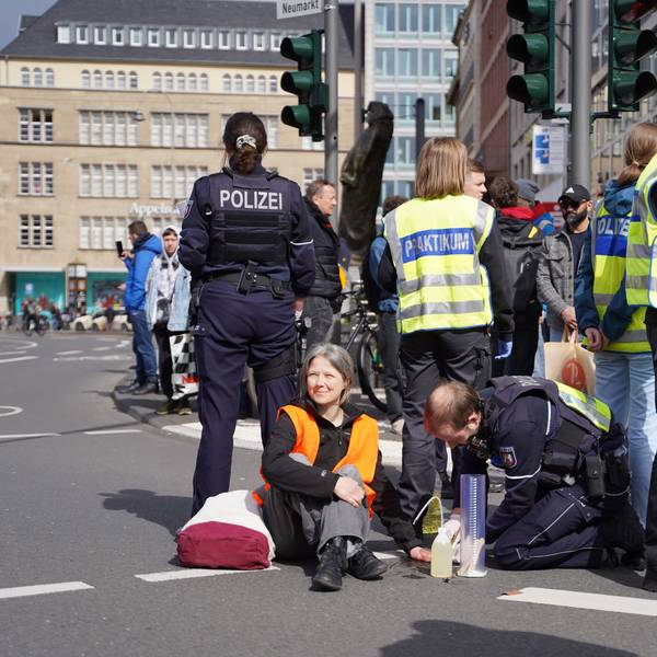 Die Polizei versucht, eine festgeklebte Aktivistin auf der Cäcilienstraße vom Asphalt zu lösen.
