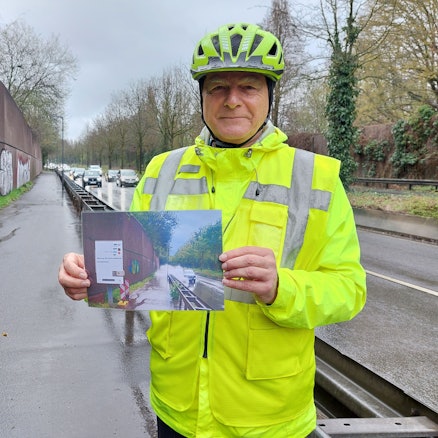 ADFC-Vorsitzender Kurt Krefft hält auf einem Radweg ein Foto derselben Stelle mit Baustelle in der Hand.