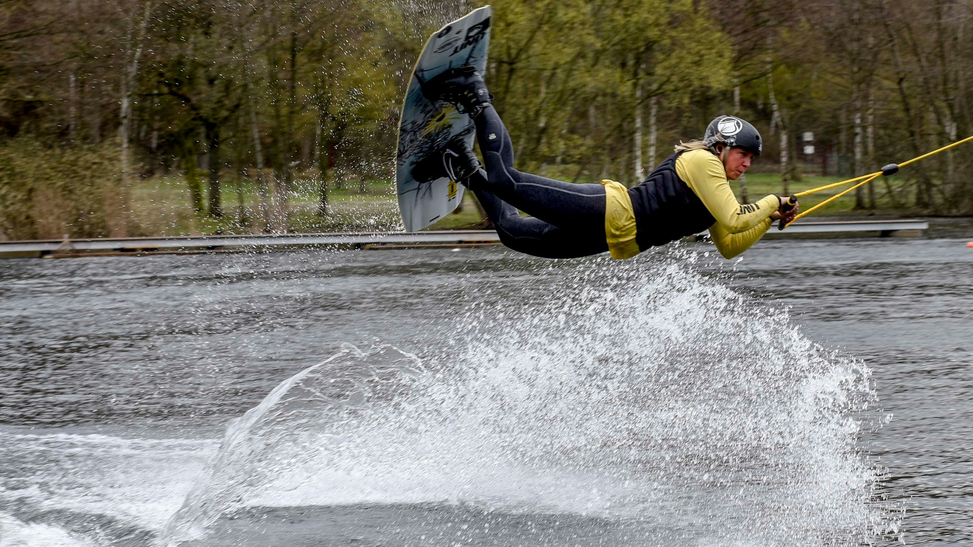 Eine Frau fährt auf einem Wakeboard an einem Seil gezogen über den See und springt auf dem Wasser.